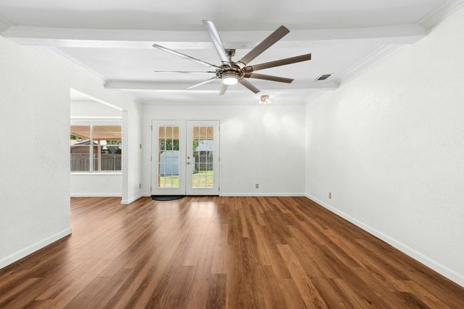 Living room with crown molding, French doors, wood finished floors, a ceiling fan, and beam ceiling | Image 6