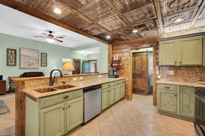 Kitchen with green cabinetry, stainless steel appliances, copper sink, ceiling fan, and a barn door into utility room. | Image 2