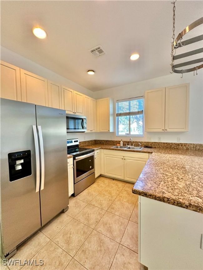 Kitchen with light stone counters, sink, light tile patterned flooring, and appliances with stainless steel finishes | Image 12