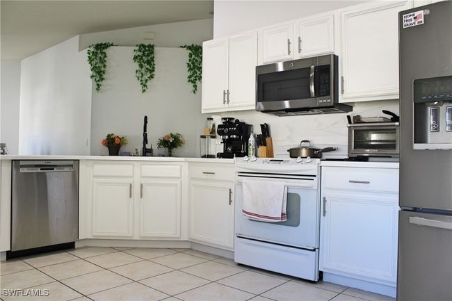 Kitchen featuring a toaster, light tile patterned floors, backsplash, appliances with stainless steel finishes, and white cabinets | Image 7