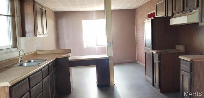 Kitchen with concrete flooring, brick wall, a sink, baseboards, and light countertops | Image 5