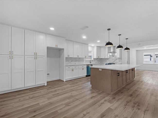 Spacious, modern kitchen with ample white cabinetry, a large island, and stylish pendant lighting. Features marble countertops, stainless steel appliances, and light wood flooring, creating an inviting and functional space. | Image 15