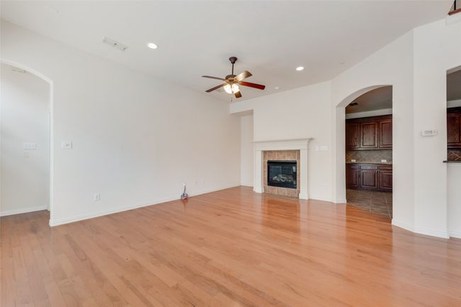 Unfurnished living room featuring a ceiling fan, light wood finished floors, a tile fireplace, recessed lighting, and arched walkways | Image 5