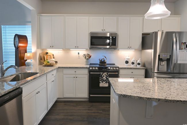 Kitchen featuring appliances with stainless steel finishes, white cabinetry, dark wood finished floors, and light stone counters | Image 7