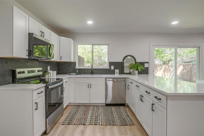 Kitchen featuring stainless steel appliances, a peninsula, light wood-style floors, backsplash, and light countertops | Image 11