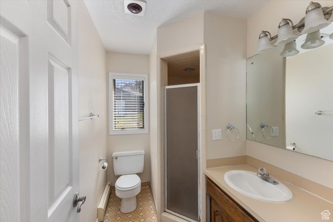 Bathroom with toilet, a baseboard radiator, a shower stall, vanity, and tile patterned flooring | Image 11
