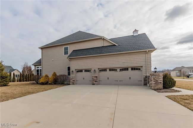 View of side of property featuring a chimney, stone siding, driveway, roof with shingles, and an attached garage | Image 20