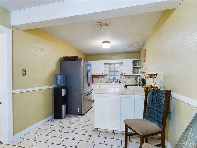 Kitchen with tasteful backsplash, stainless steel refrigerator, light tile floors, white cabinetry, and tile countertops | Image 11