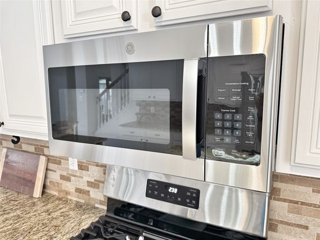 Kitchen view of backsplash, white cabinets, stainless steel microwave, multiple ovens, and light stone countertops | Image 18