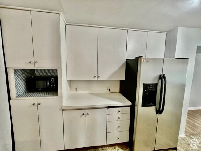 Kitchen with baseboards, black microwave, light countertops, white cabinetry, and stainless steel refrigerator with ice dispenser | Image 10