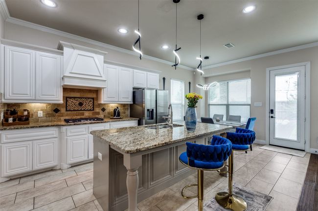 Kitchen with stainless steel appliances, custom range hood, an island with sink, tasteful backsplash, and light stone countertops | Image 8
