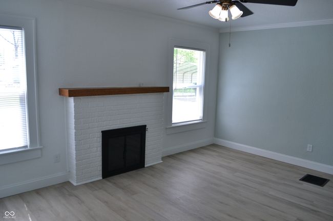 Living room with a wood burning fireplace, a ceiling fan, ornamental molding, and vinyl plank flooring | Image 12