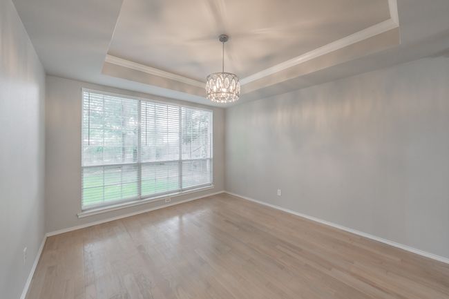 Unfurnished room with a raised ceiling, a chandelier, ornamental molding, light wood-type flooring, and baseboards | Image 11