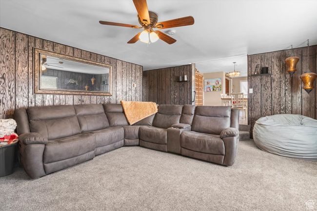 Carpeted living room with wood walls and ceiling fan with notable chandelier | Image 28