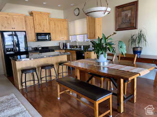 Kitchen with light brown cabinetry, dark wood-style floors, black appliances, dark countertops, and a kitchen bar | Image 8