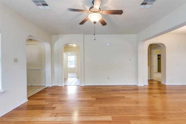 Empty room with ceiling fan, light wood-style floors, and arched walkways | Image 7