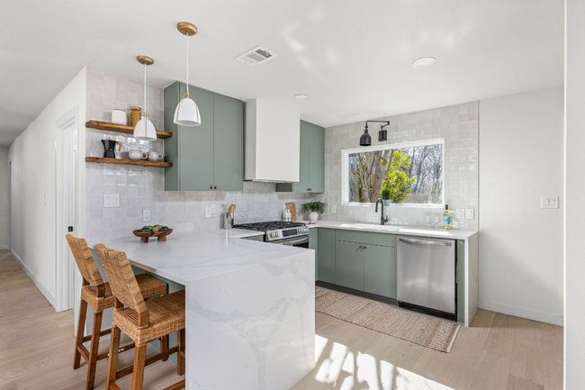 Kitchen with stainless steel appliances, green cabinets, a peninsula, light wood-style floors, and backsplash | Image 13