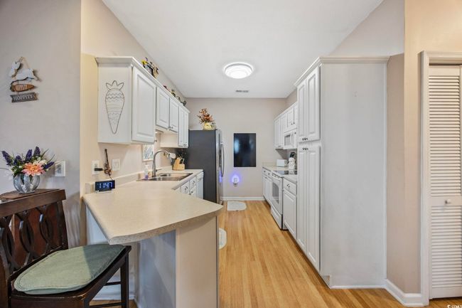 Kitchen featuring a sink, white appliances, light countertops, a breakfast bar, and light wood-style floors | Image 10