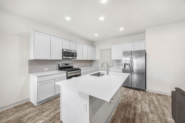 Another view of the gourmet kitchen, highlighting the ample counter space, subway tile backsplash, and a large side-by-side refrigerator, all with a bright and clean aesthetic. | Image 13