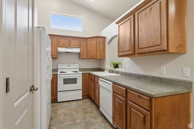 Kitchen featuring white appliances, under cabinet range hood, a sink, brown cabinetry, and high vaulted ceiling | Image 16