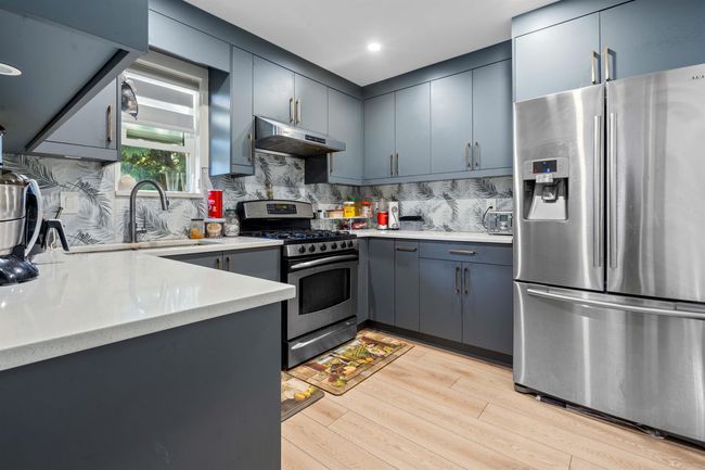 Kitchen featuring under cabinet range hood, light countertops, a sink, light wood-style flooring, and appliances with stainless steel finishes | Image 30