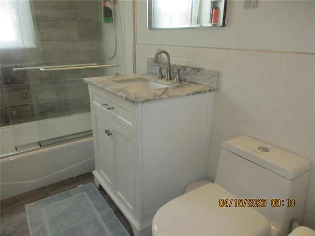 Bathroom featuring toilet, tile walls, enclosed tub / shower combo, vanity, and wood finished floors | Image 15