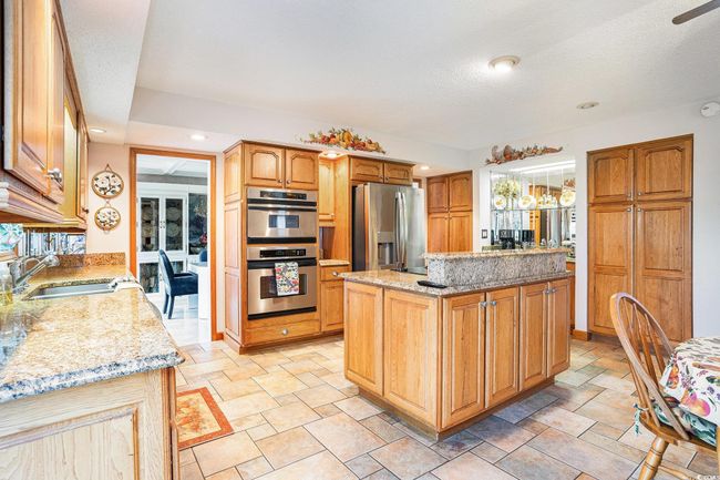 Kitchen with appliances with stainless steel finishes, a sink, light stone countertops, light stone finish flooring, and a center island | Image 9