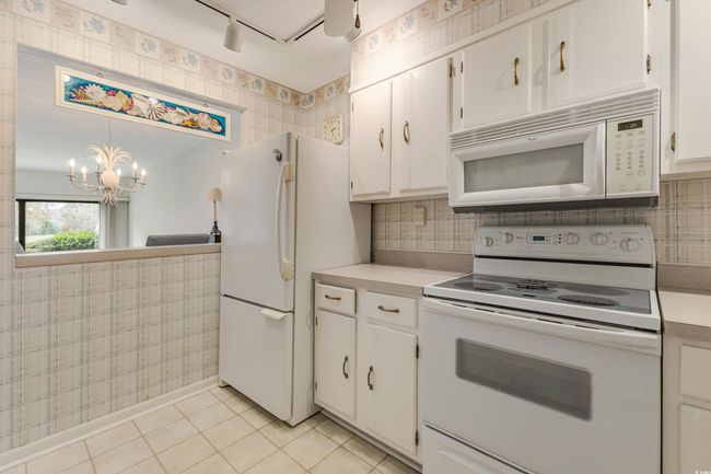 Kitchen with white cabinets, light countertops, a notable chandelier, and white appliances | Image 8
