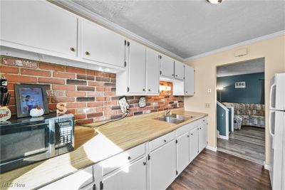 Kitchen with white cabinets, sink, white fridge, crown molding, and dark hardwood / wood-style flooring | Image 2