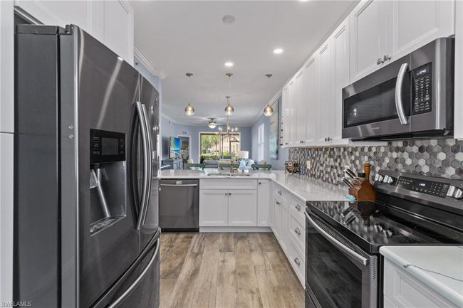 Kitchen featuring decorative light fixtures, ornamental molding, appliances with stainless steel finishes, kitchen peninsula, and white cabinets | Image 5