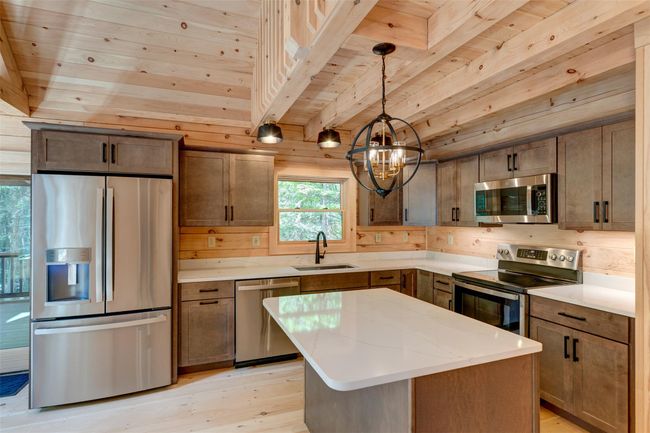 Kitchen with stainless steel appliances, wood ceiling with exposed beams, light wood finished floors, a sink, and wood walls | Image 15
