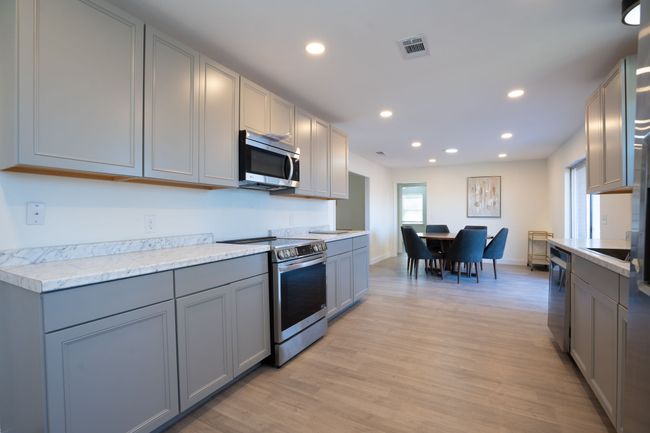 Kitchen with stainless steel appliances, gray cabinets, recessed lighting, light countertops, and light wood finished floors | Image 15