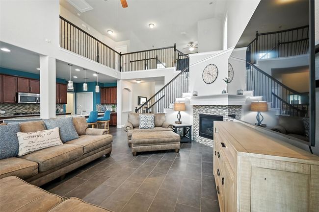 Living area featuring a ceiling fan, a high ceiling, stairway, a tiled fireplace, and dark tile patterned floors | Image 7