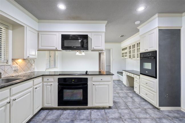 Kitchen featuring black appliances, a peninsula, backsplash, white cabinets, and ornamental molding | Image 10