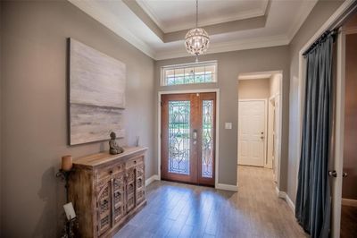 Elegant entryway with a high ceiling, decorative light fixture, ornate wooden console, and a welcoming front door with glass inserts. | Image 3