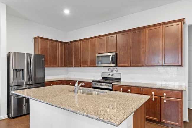 Kitchen with light stone countertops, a sink, backsplash, and appliances with stainless steel finishes | Image 10
