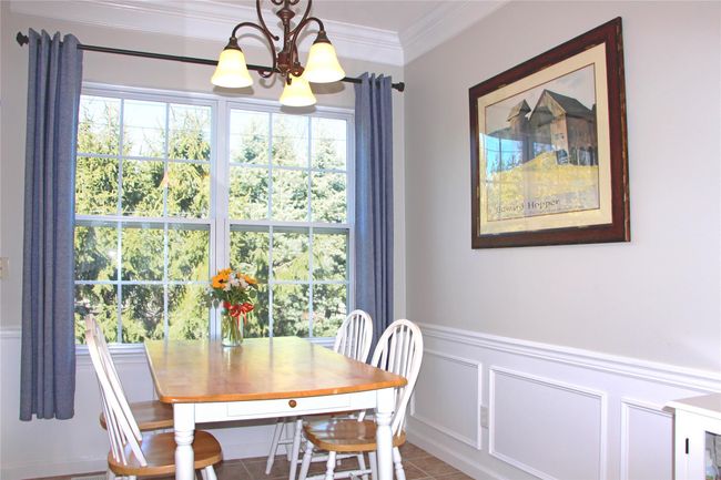 Dining room with a decorative wall, ornamental molding, light tile patterned floors, wainscoting, and a notable chandelier | Image 11