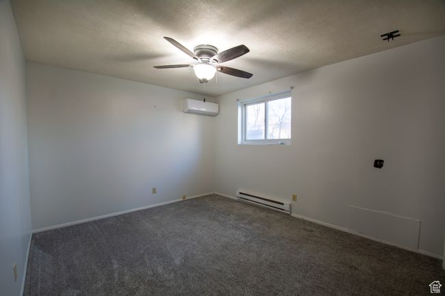 Spare room featuring a wall mounted air conditioner, dark colored carpet, ceiling fan, baseboard heating, and a textured ceiling | Image 13
