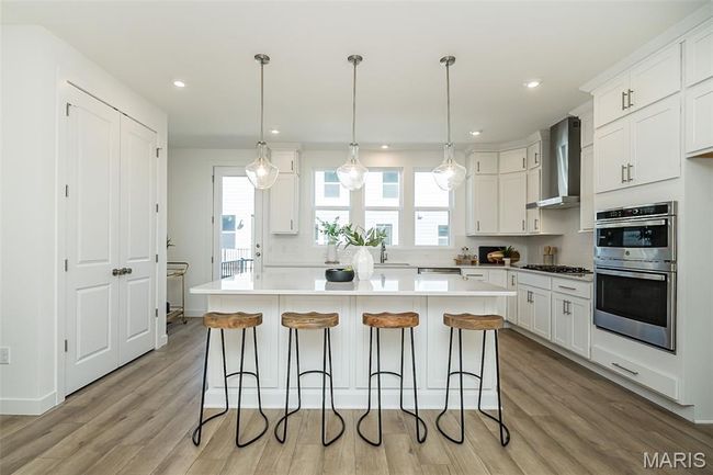 Kitchen with white cabinets, wall chimney range hood, light wood-style floors, a breakfast bar area, and recessed lighting | Image 5