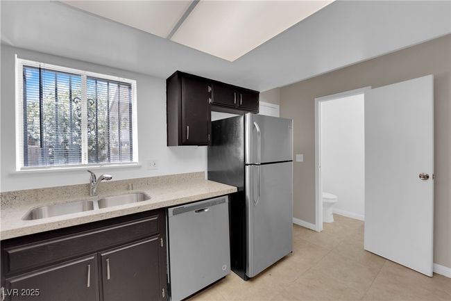 Kitchen with appliances with stainless steel finishes, a sink, light tile patterned floors, baseboards, and light stone counters | Image 10