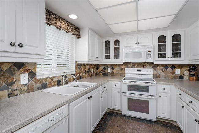 Kitchen with white cabinetry, a sink, white appliances, and glass insert cabinets | Image 16