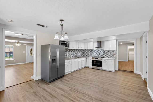 Kitchen with appliances with stainless steel finishes, wall chimney exhaust hood, white cabinets, light wood-style floors, and a textured ceiling | Image 25