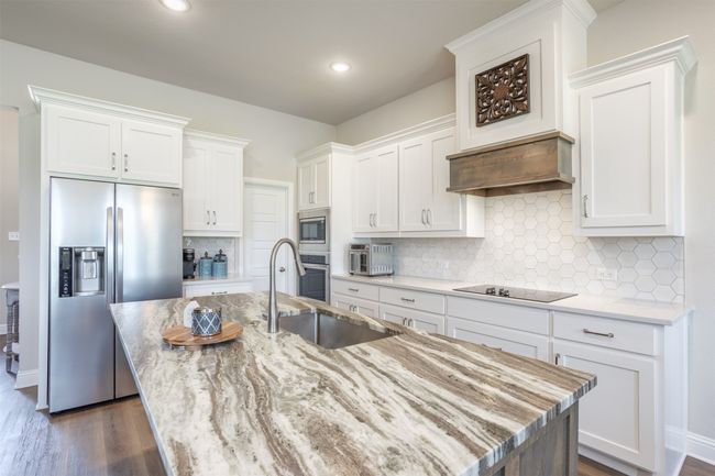 The large kitchen has beautiful Fantasy Brown Marble Countertops on the island paired with coordinating quartz. Decorative Cooktop Vent and a pantry that will be the envy of your neighbors. | Image 7