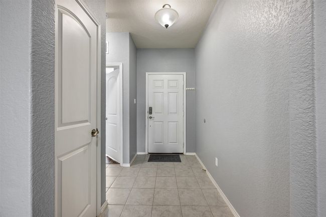 Doorway to outside featuring a textured wall, baseboards, and light tile patterned floors | Image 5