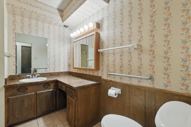 Bathroom with wallpapered walls, wainscoting, toilet, tile patterned floors, and vanity | Image 29
