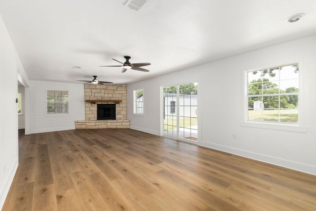 Spacious family room featuring a cozy stone fireplace, elegant floors, and abundant natural light from large windows and sliding glass doors. Perfect for gatherings and relaxation. | Image 26