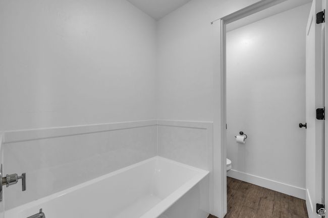 Full bathroom with a bath, toilet, baseboards, and wood finished floors | Image 16