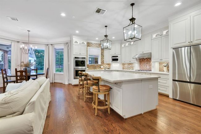 Flowing effortlessly from the family room is the gourmet kitchen, anchored by a large granite island with a leather finish, offering bar seating and additional storage. Overhead, two classic lantern-style pendant lights provide timeless charm. | Image 12
