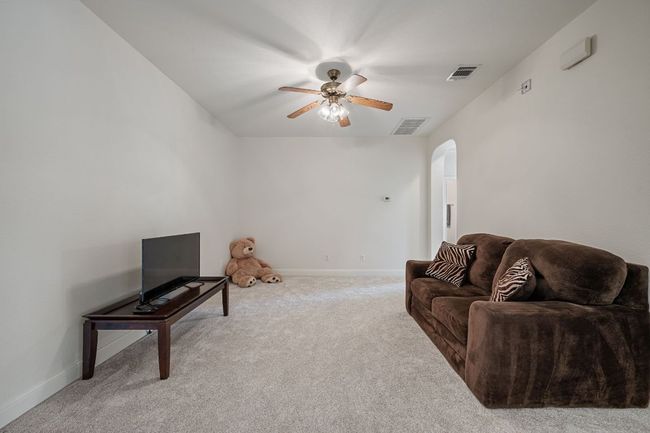 Carpeted living room featuring baseboards, visible vents, arched walkways, and a ceiling fan | Image 25