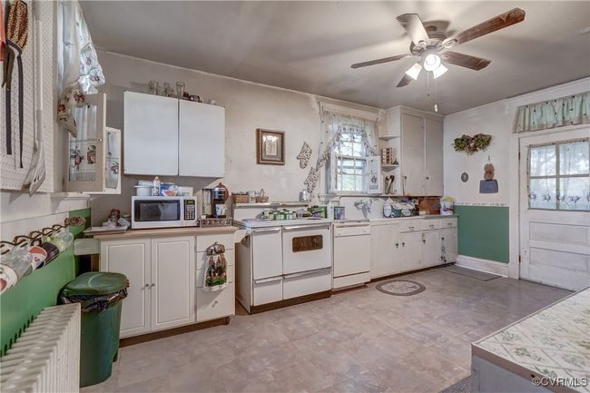 Kitchen with white appliances, ceiling fan, radiator heating unit, white cabinetry, and open shelves | Image 11
